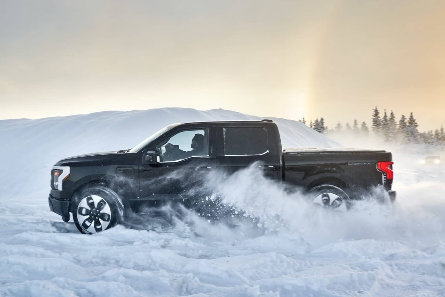 A 2022 Ford F-150 Lightning truck driving through a snowy countryside.