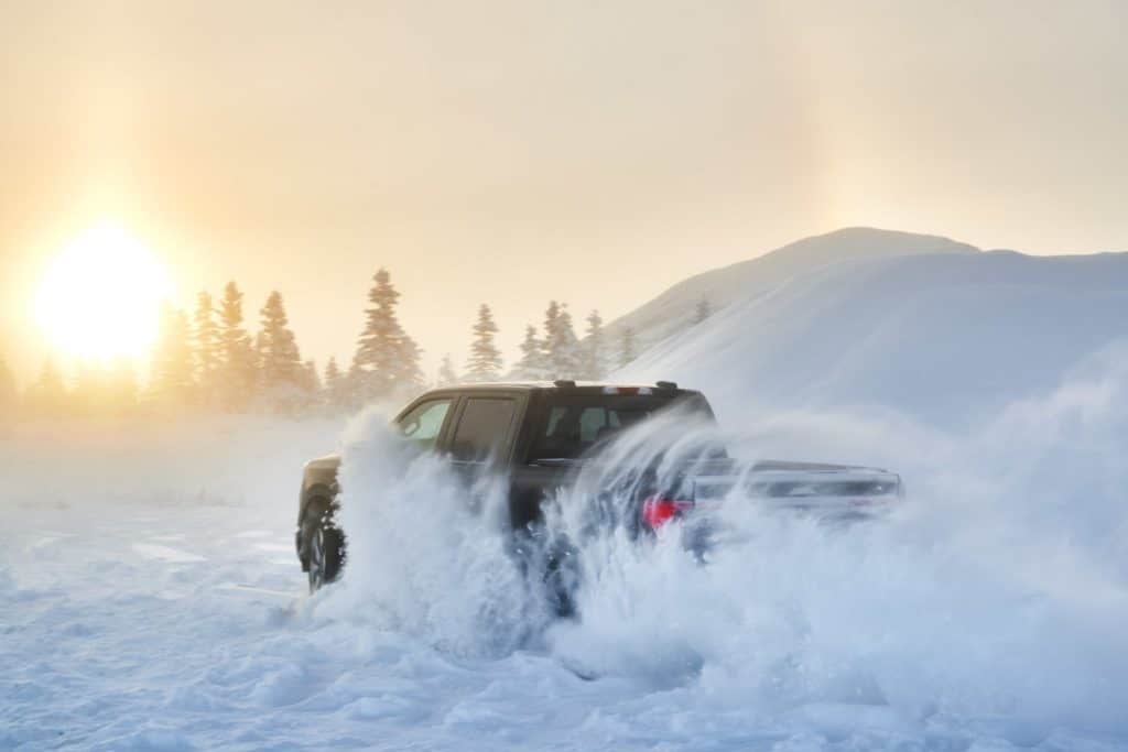 A 2022 Ford F-150 Lightning truck driving through a snowy countryside.