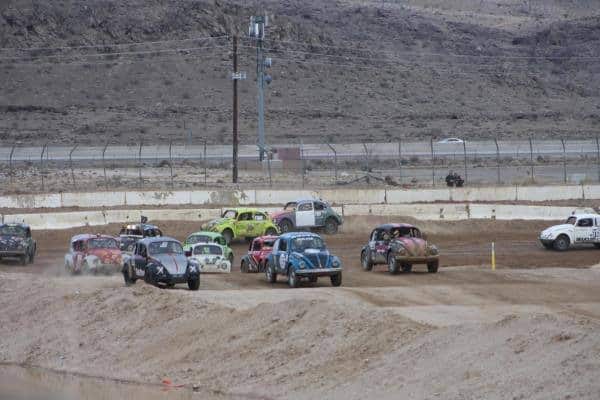 Many VW Bettles racing around a dirt track.