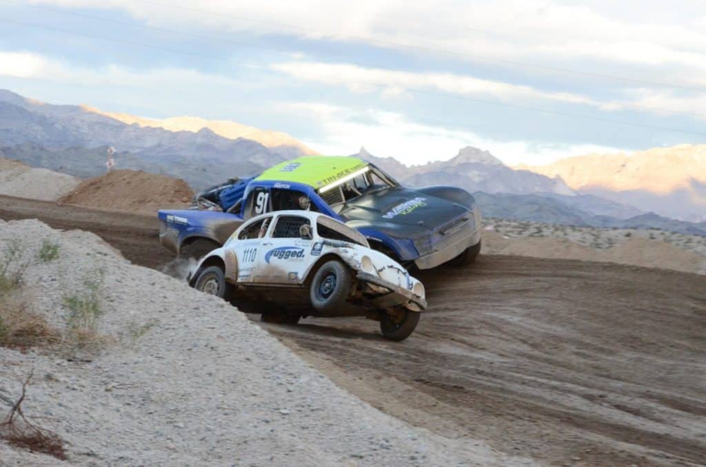 A VW Bettle and a racing truck taking a corner.