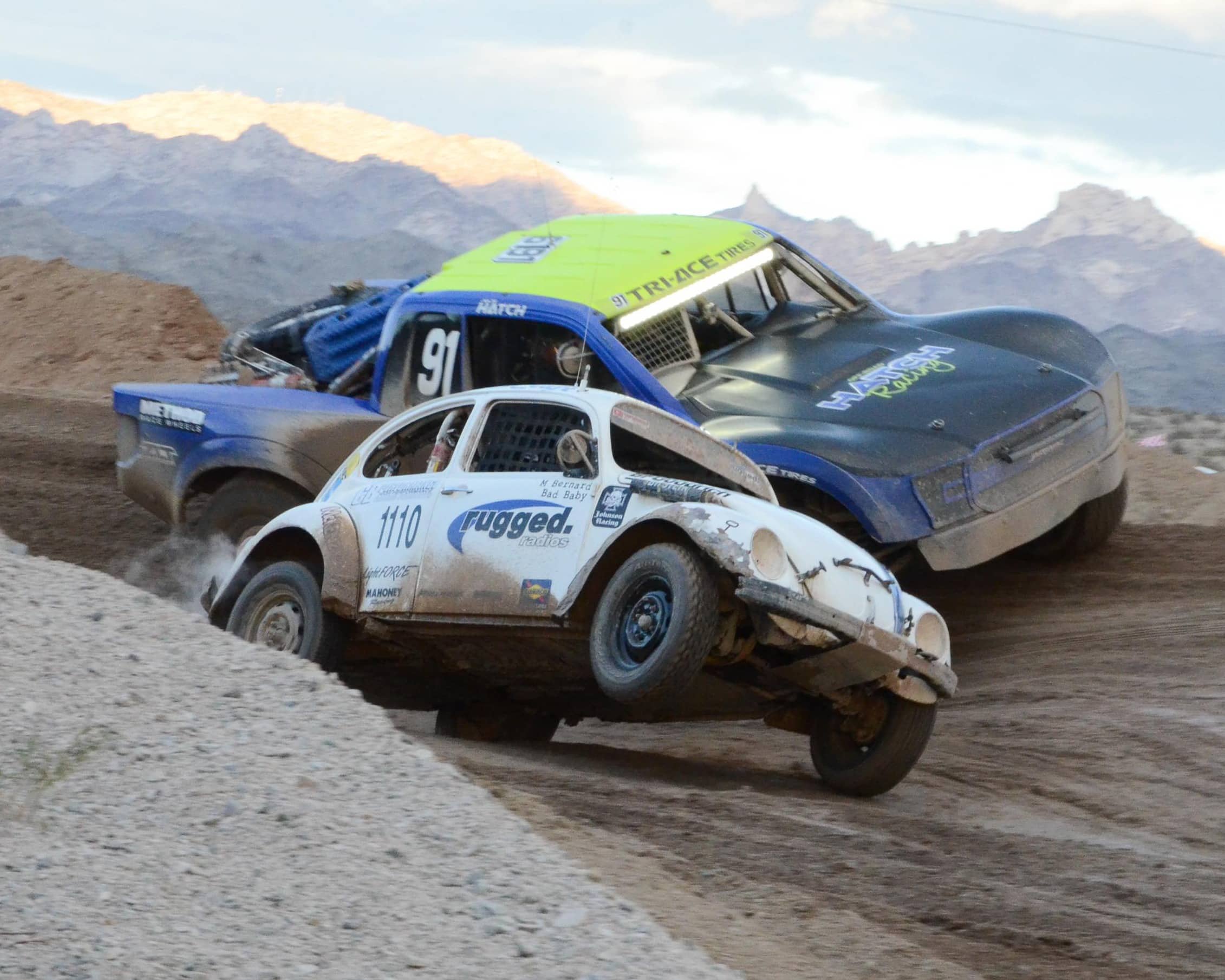 A VW Bettle racing a truck around a dirt track.