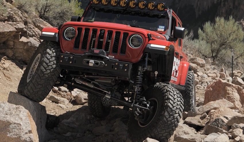 A red Jeep Gladiator driving over a rocky hillside.