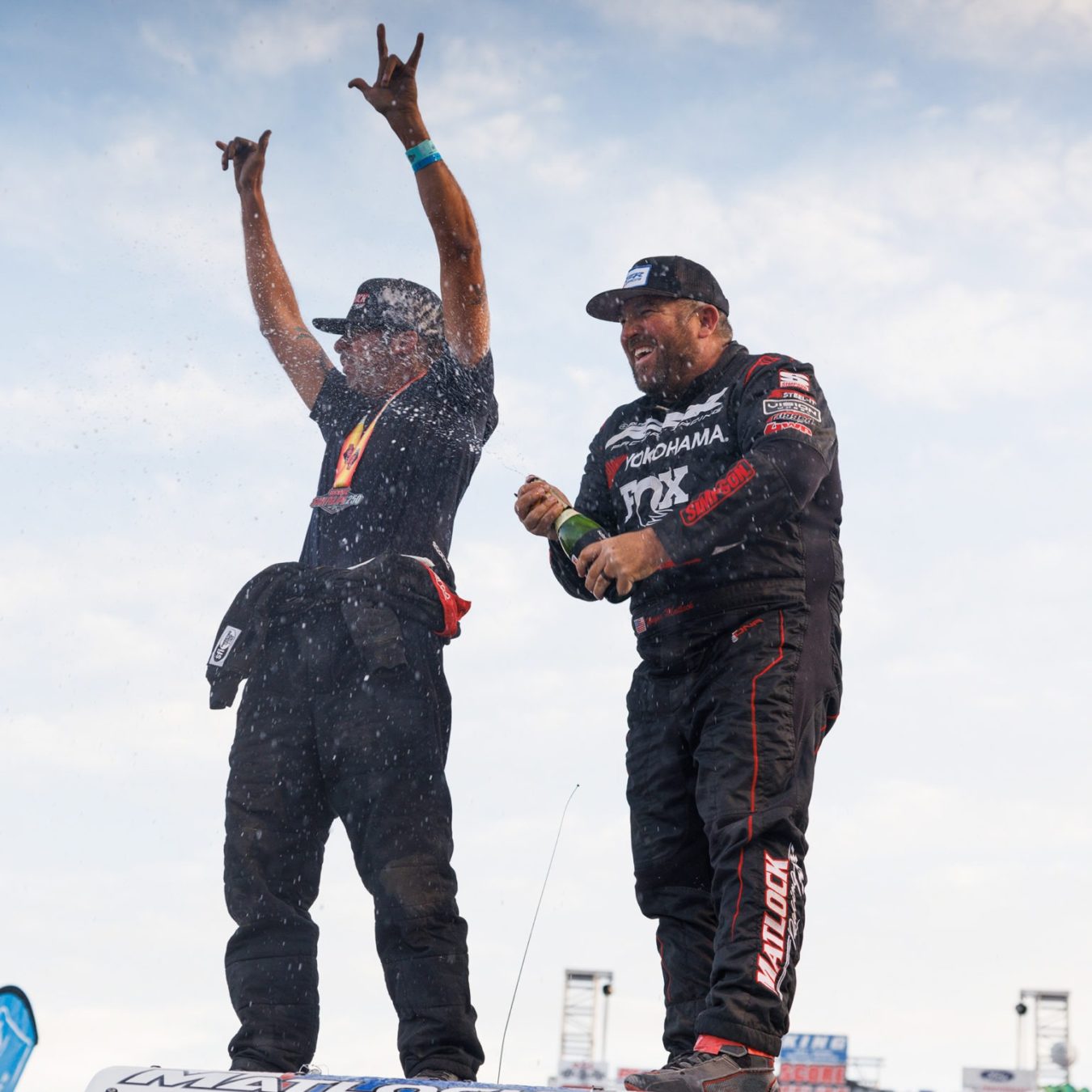 Two men popping a bottle of champagne in celebration of their race win.