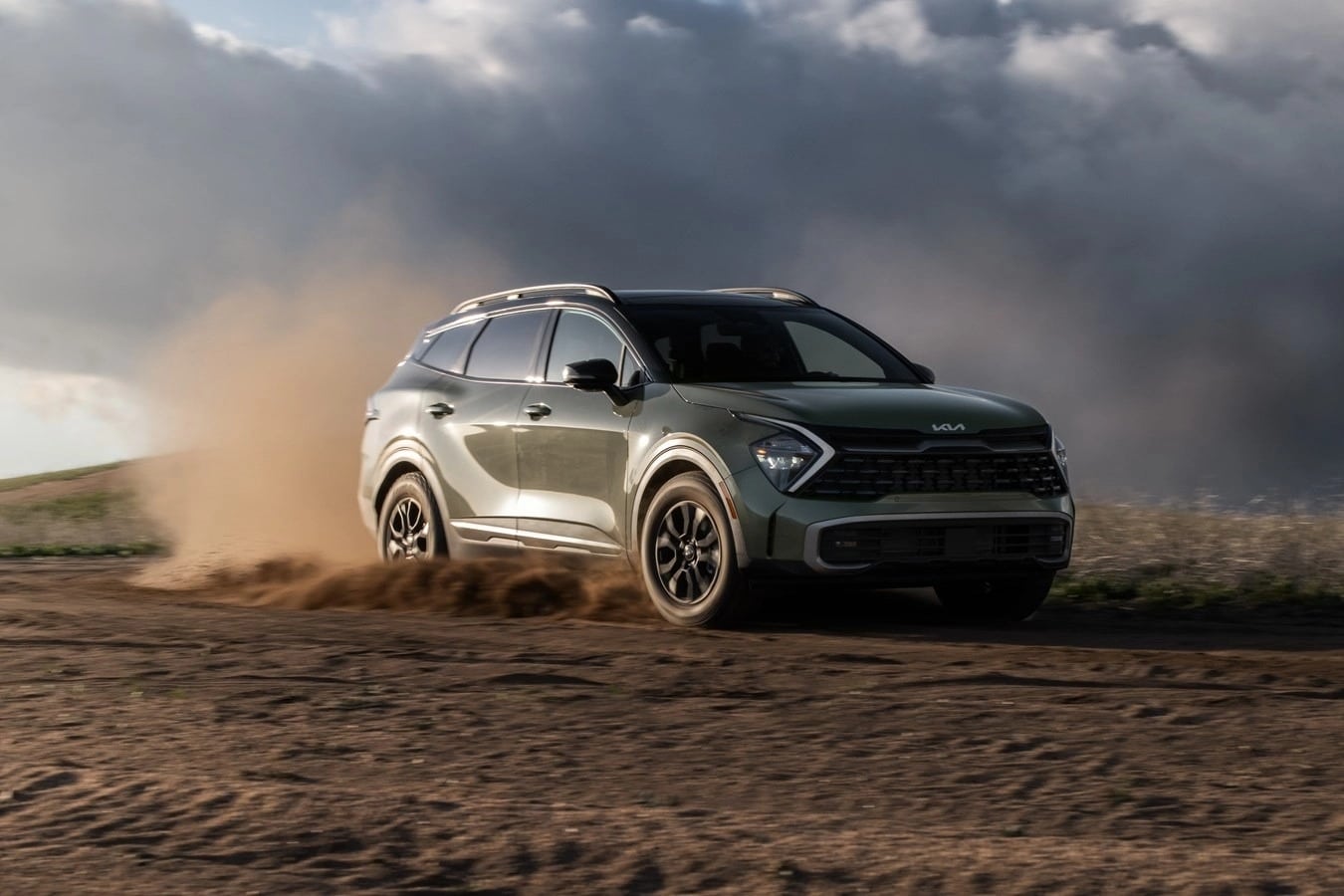 A Kia Sportage X driving across a desert area, throwing sand and clouds of dirt into the air.