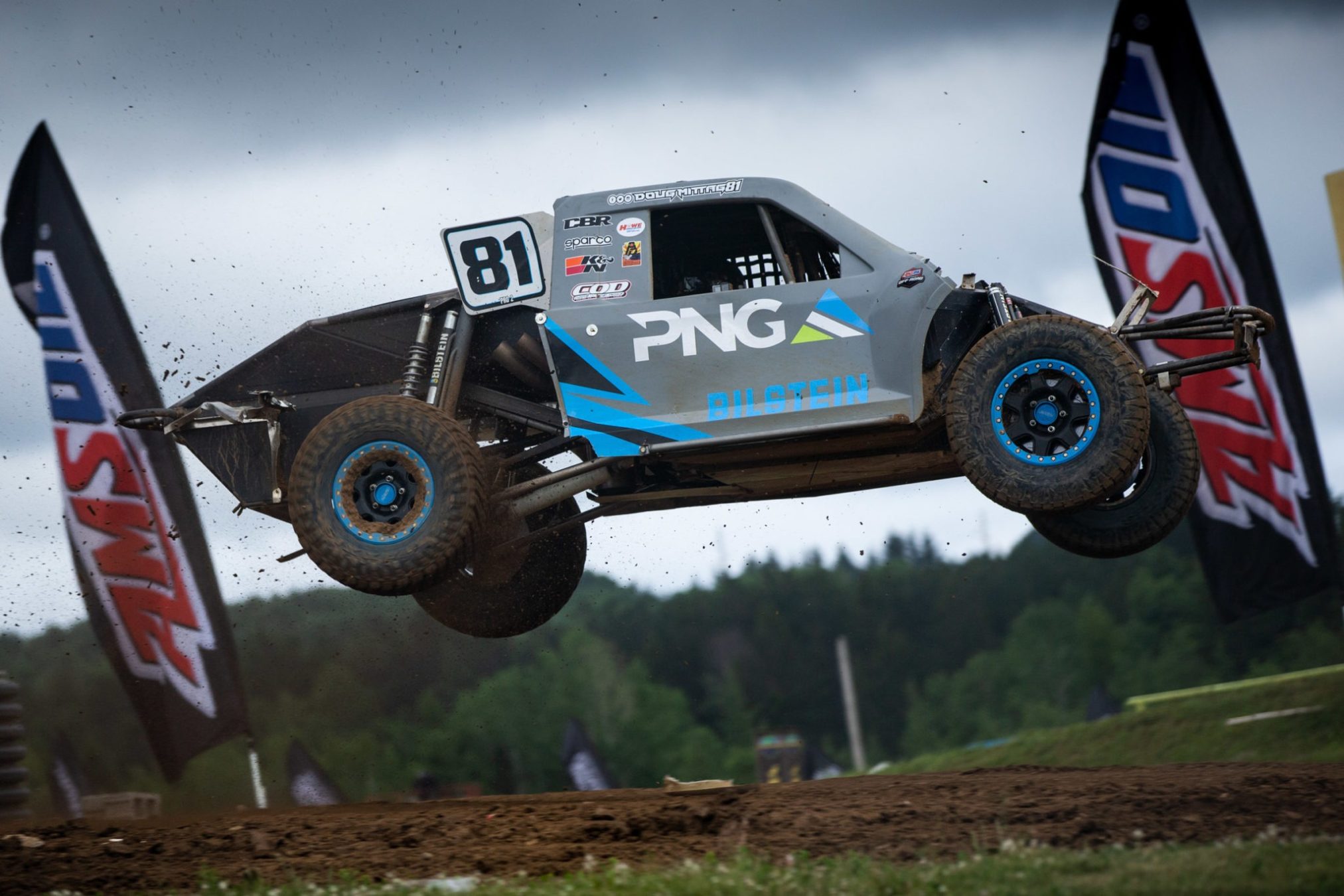 A racing truck jumping off a dirt track ramp.