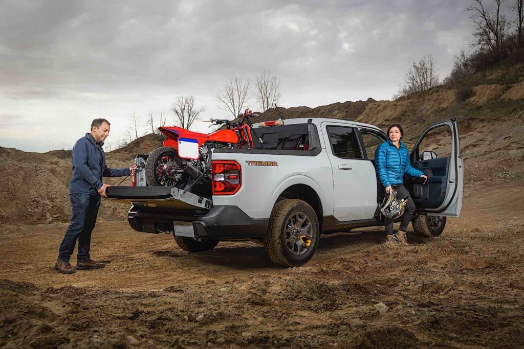 A man unloads drops the tailgate of a 2023 Ford Maverick while a woman steps out of the passenger side door.