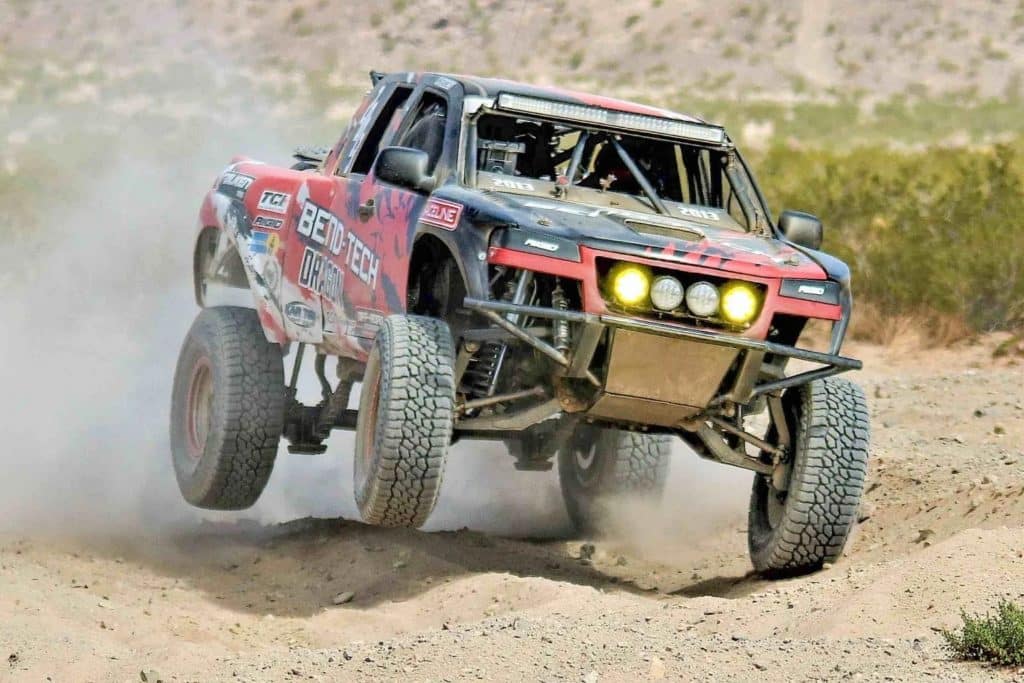 An off-road racing truck spraying dirt into the air as it drives through the desert.