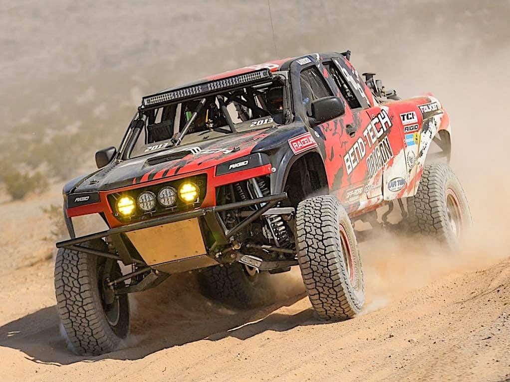An off-road racing truck spraying dirt into the air as it drives through the desert.
