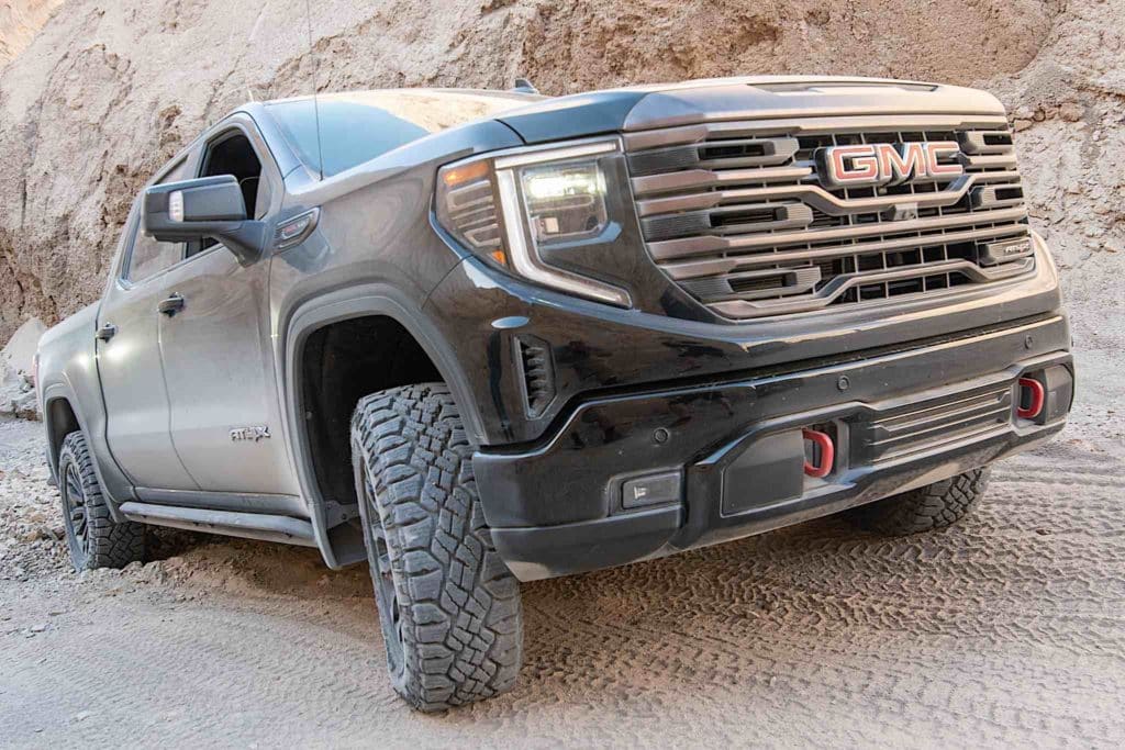 A GMC Sierra AT4X driving across rocky desert terrain.