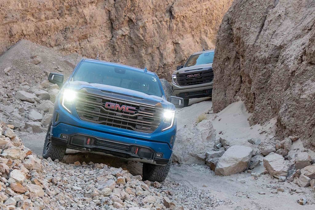 A GMC Sierra AT4X driving across rocky desert terrain.