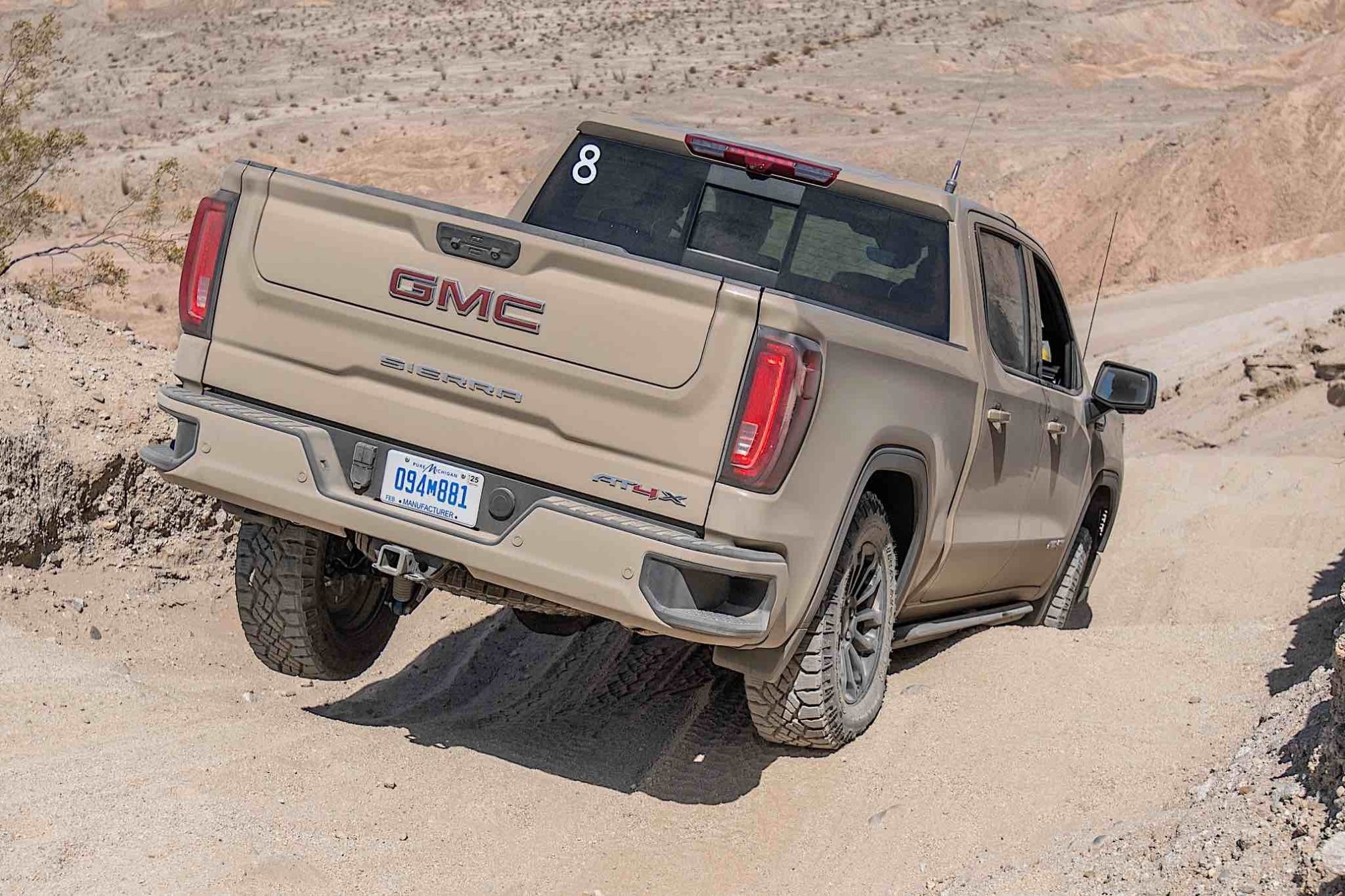 A brown GMC Sierra AT4X driving across rocky desert terrain.