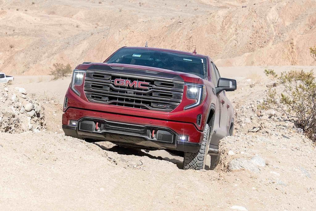 A red GMC Sierra AT4X driving across rocky desert terrain.