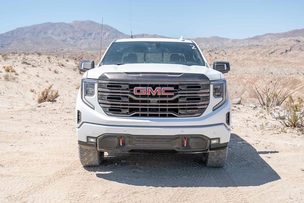 A white GMC Sierra AT4X driving across rocky desert terrain.