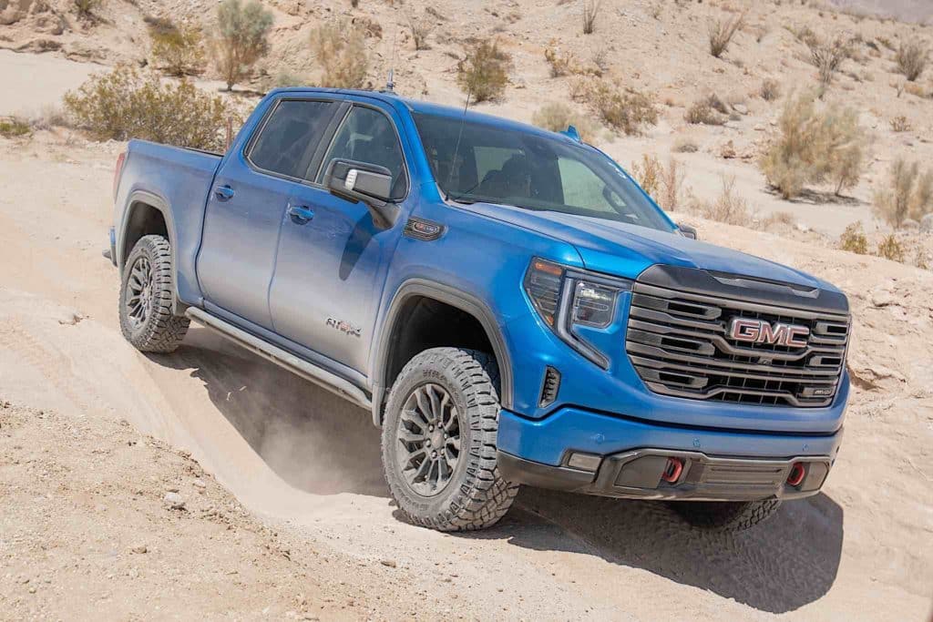 A GMC Sierra AT4X driving across rocky desert terrain.