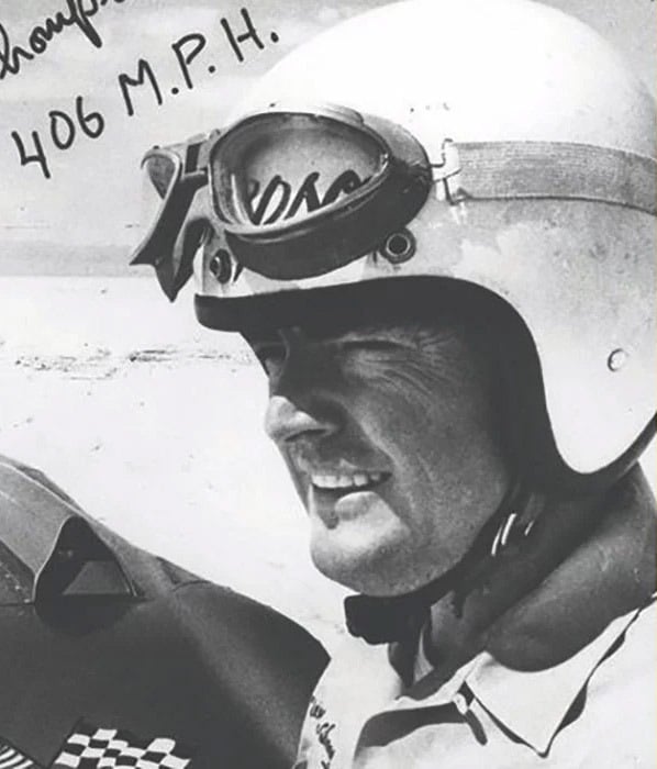 A black and white photo of Mickey Thompson wearing racing gear.