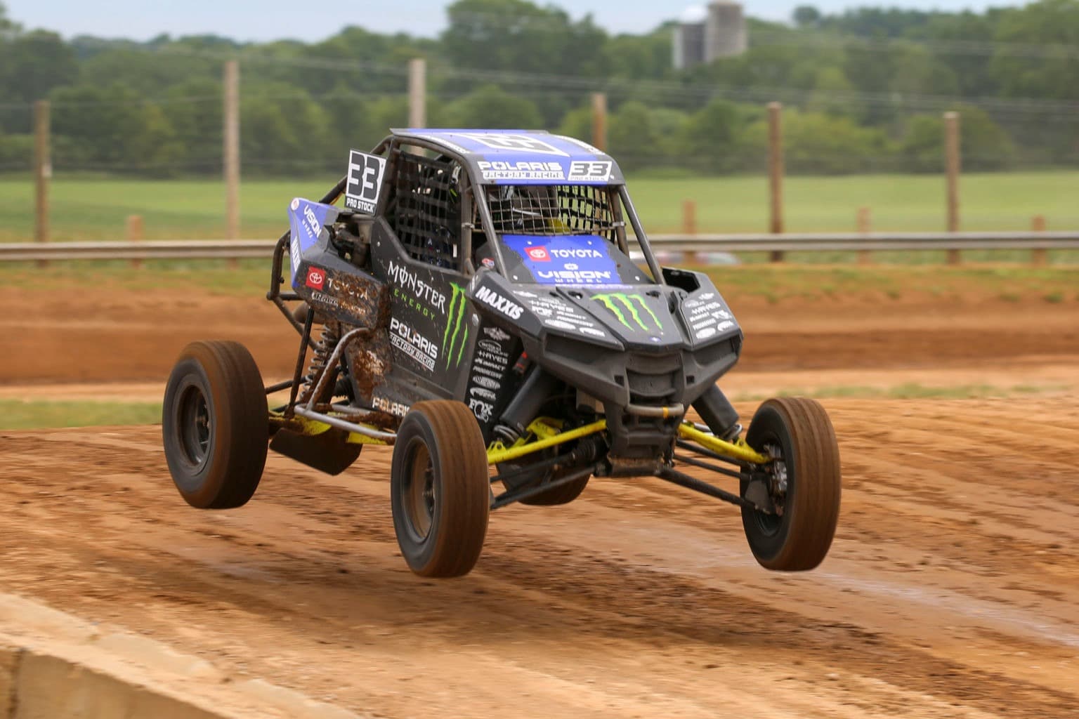 A racing truck leaping through the air on a dirt racing track.