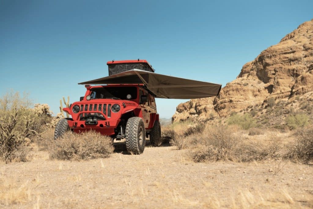 A red jeep parked next to a rock structure in the desert.
