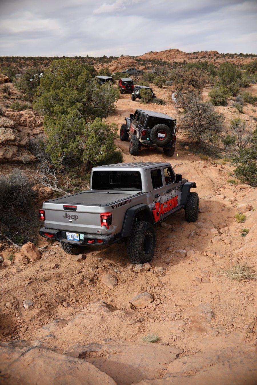 A caravan of jeeps and trucks driving across dirty terrain.