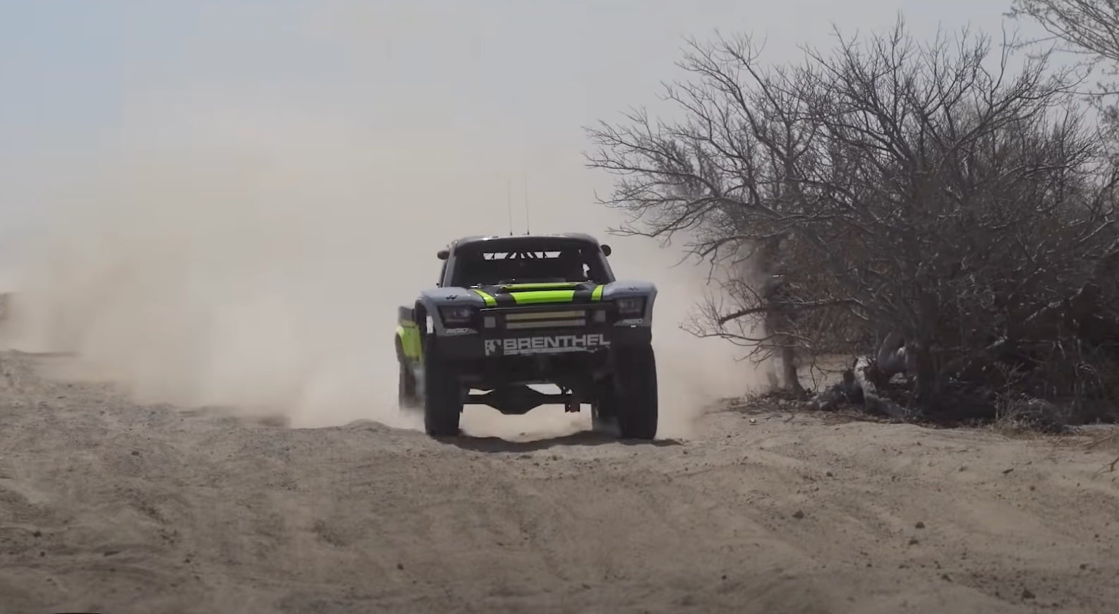 A trophy truck racing down Zoo Road, throwing dust and clouds of dirt up behind it.