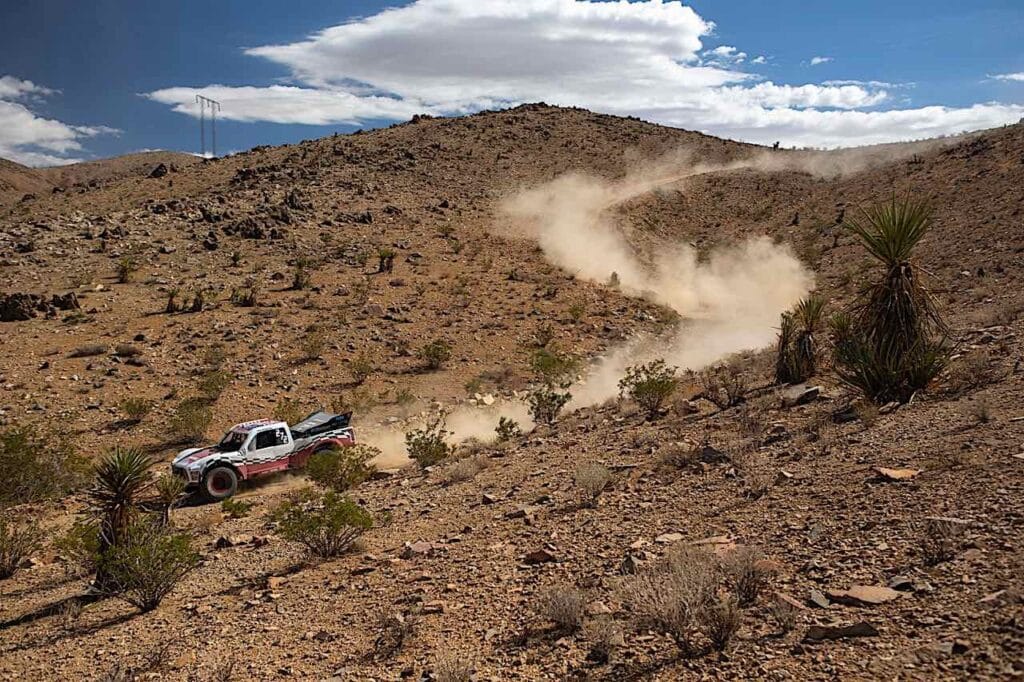 A truck racing down a hill leaving dirt clouds in its tracks.