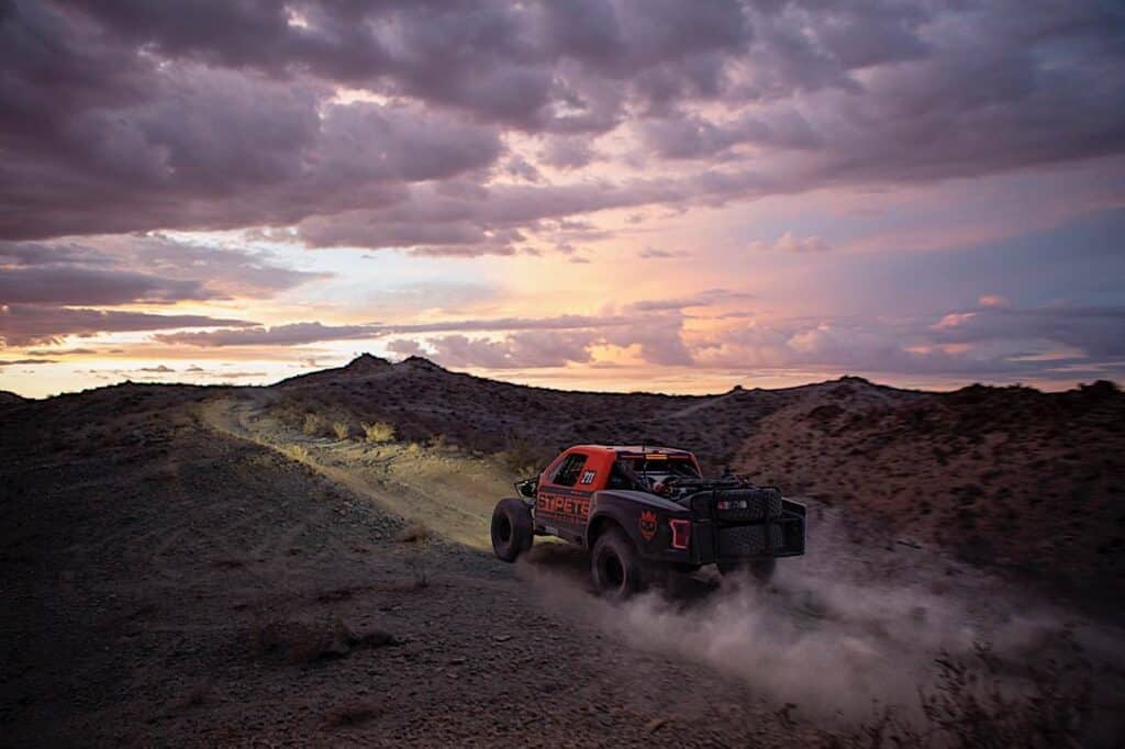 A dirt-track racing vehicle driving across a track near sunset.