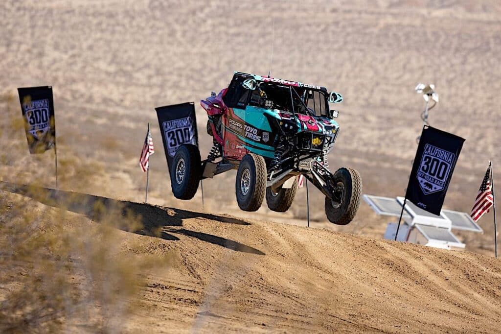 A racing vehicle jumping off a dune on the track.